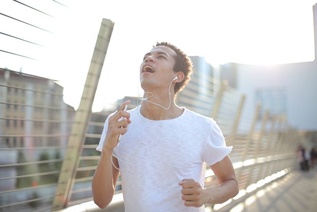 A young man running outdoors on a sunny day, enjoying music through earbuds.