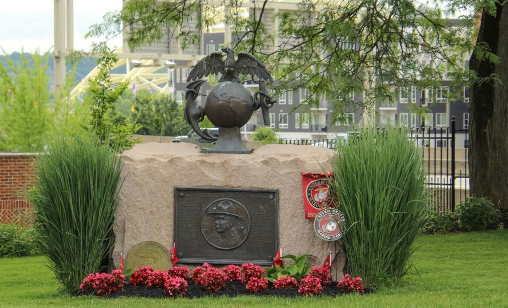 A memorial displaying the US Marine Corps emblem surrounded by greenery and flowers.