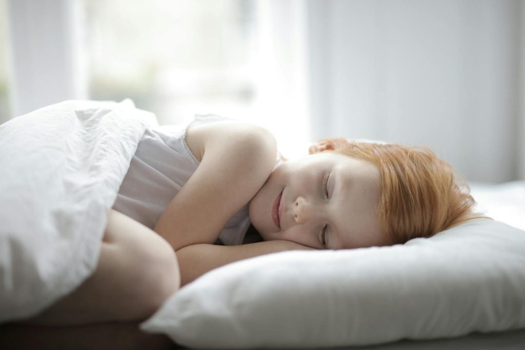 A young girl peacefully sleeping in a bright bedroom, conveying comfort and relaxation.