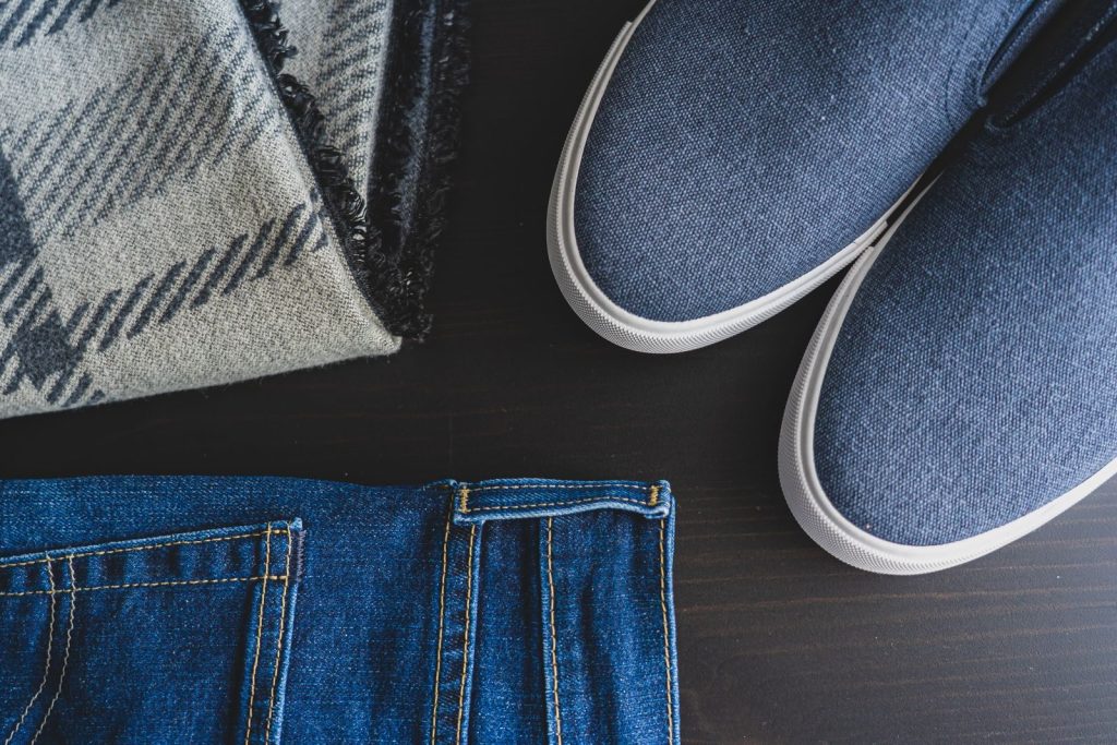 Flat lay of denim jeans, blue sneakers, and a plaid scarf for a casual look.