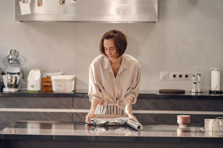 A focused woman wraps food in aluminum foil in a sleek, modern kitchen.