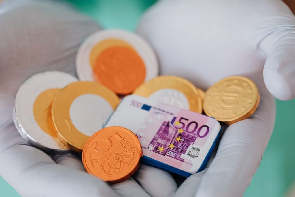 Unrecognizable medical practitioner demonstrating plastic money euro and coins in gloves in clinic while working and holding money wearing medical uniform