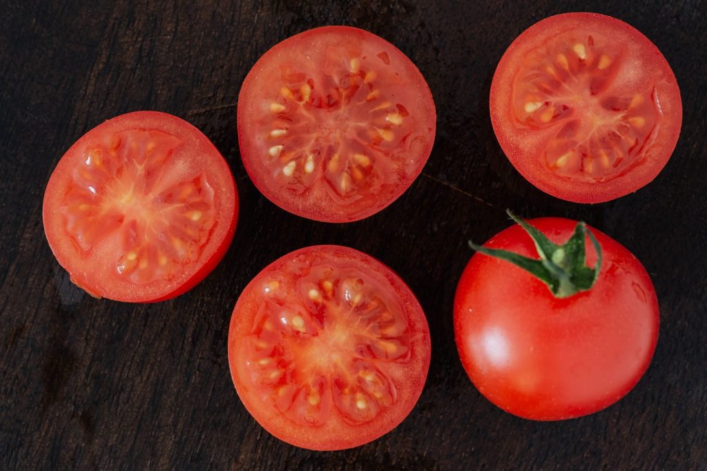 Top view of appetizing ripe red tomato with green tail placed near ripe juicy halves of tomatoes arranged on wooden board