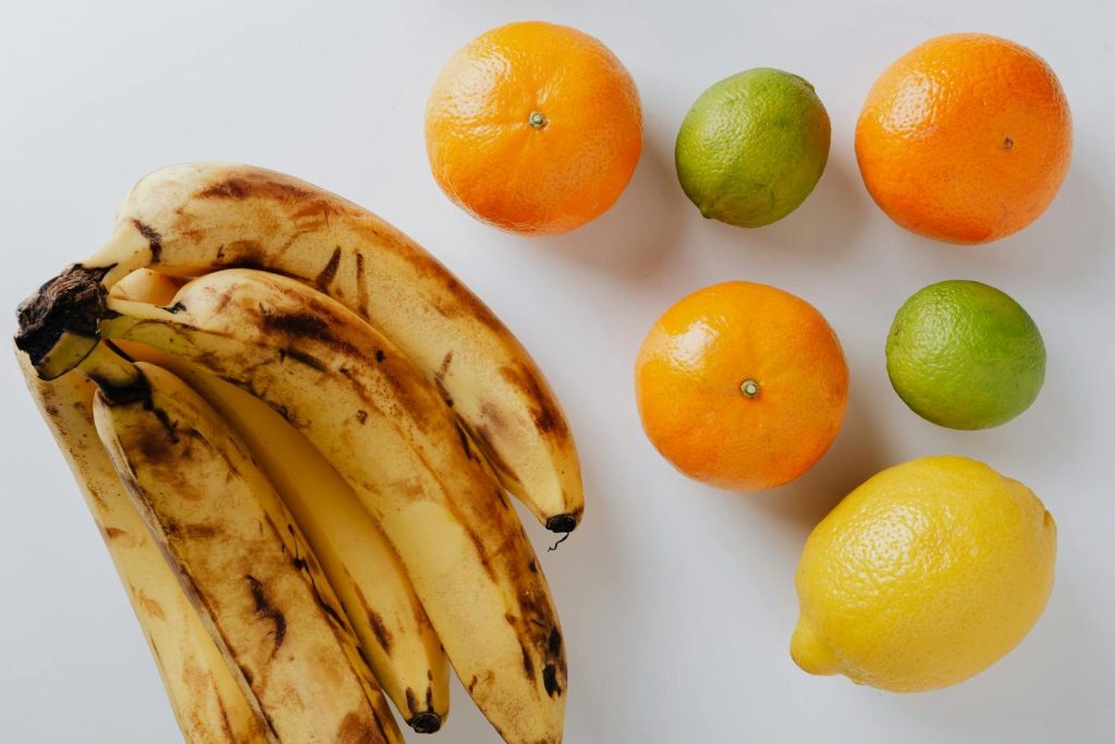 A vibrant arrangement of ripe bananas, oranges, limes, and a lemon on a clean white background.