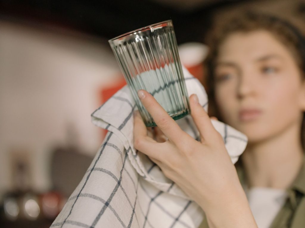 Young woman dries a glass with a towel, emphasizing cleanliness and domesticity at home.