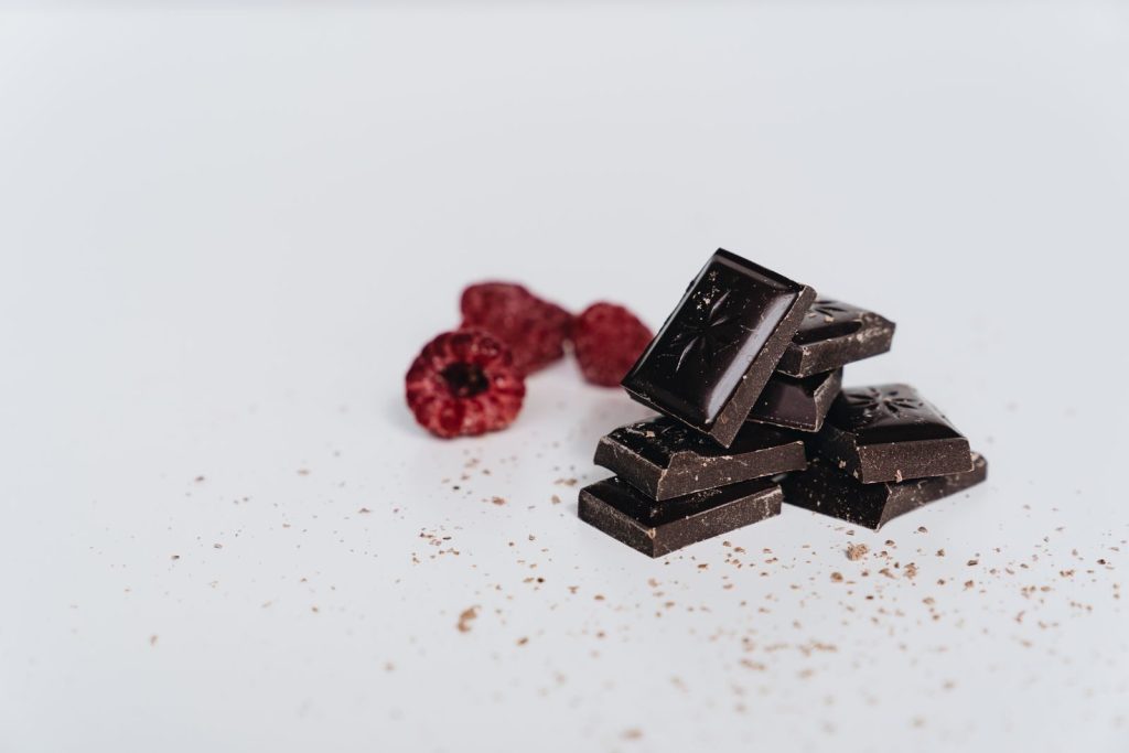 Artistic shot of dark chocolate pieces and fresh raspberries on a white backdrop.