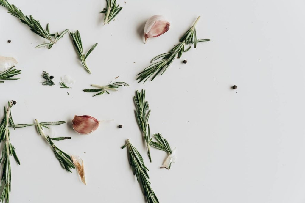Aromatic rosemary, garlic, and peppercorns artfully arranged on a white surface.