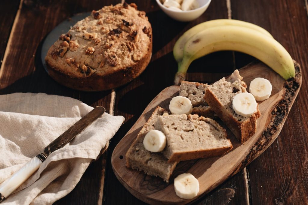 A rustic presentation of homemade banana bread with fresh bananas on a wooden board.
