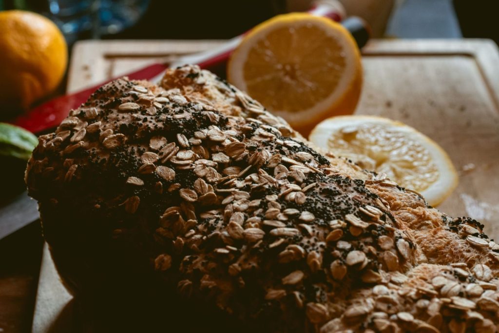Close-up of rustic bread with oat toppings and lemon slices on a wooden board.