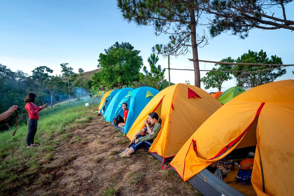 Side view of unrecognizable travelers spending time in camp with colorful tents in countryside