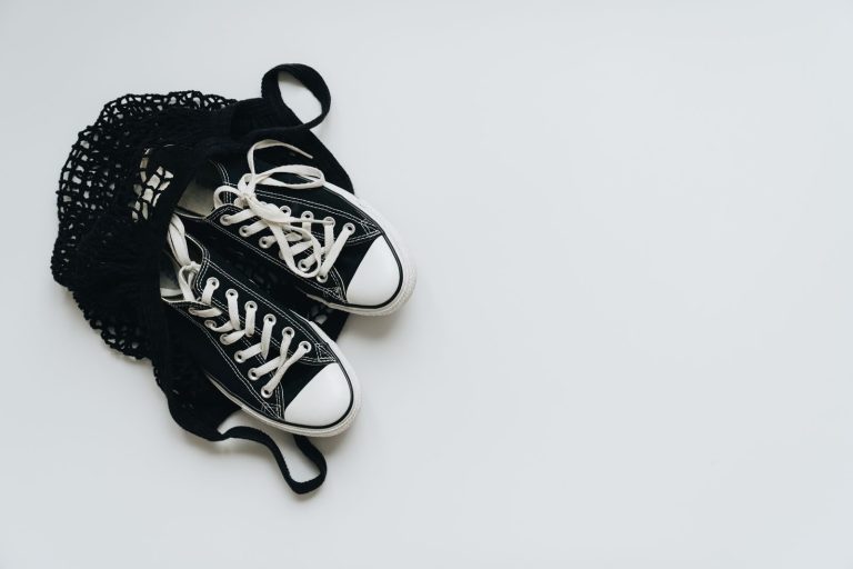 A pair of classic black sneakers in a black net bag on a white background, showcasing minimalism.