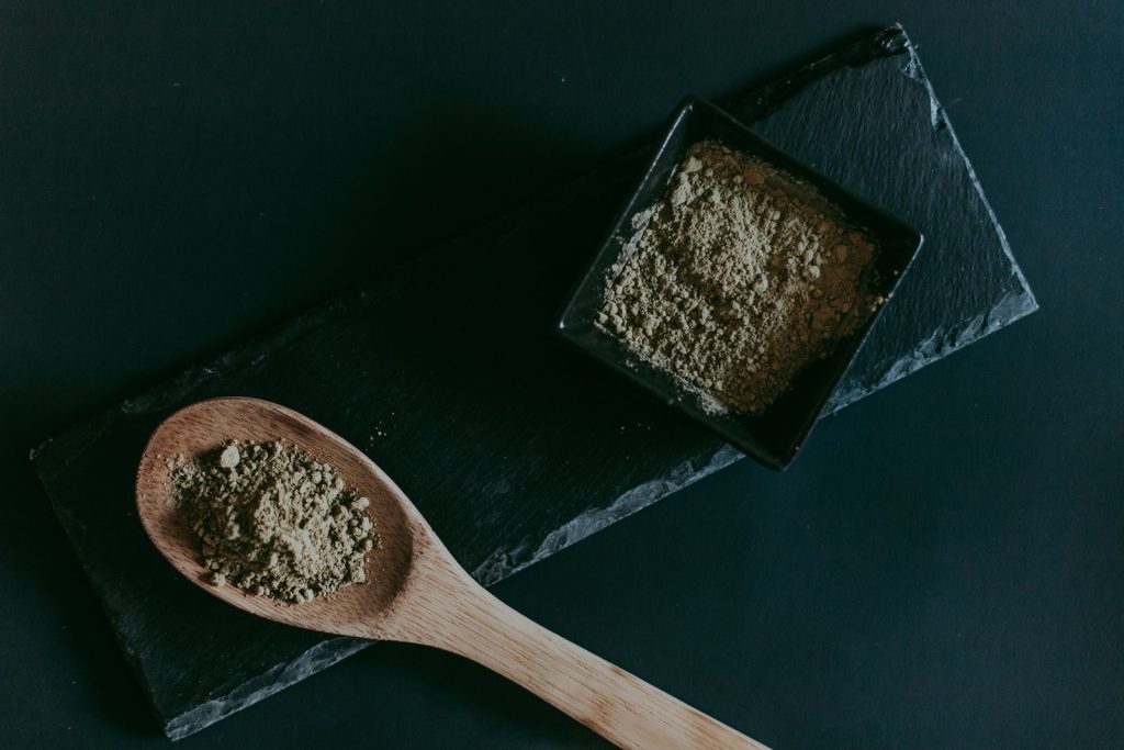 Overhead shot of brown sugar in a wooden spoon and black ceramic bowl on dark slate.