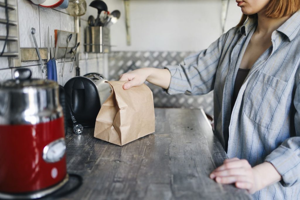 Woman in kitchen placing a brown paper bag of food on the counter, showcasing modern kitchenware.