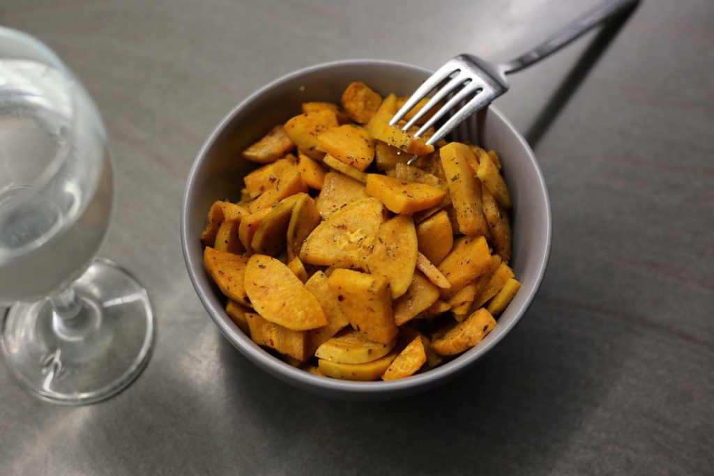 From above sliced fried sweet potato served in ceramic bowl with fork and glass of water on table