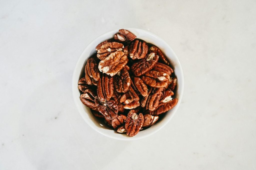 Top view of a bowl filled with healthy pecan nuts on a light surface, ideal for nutrition themes.