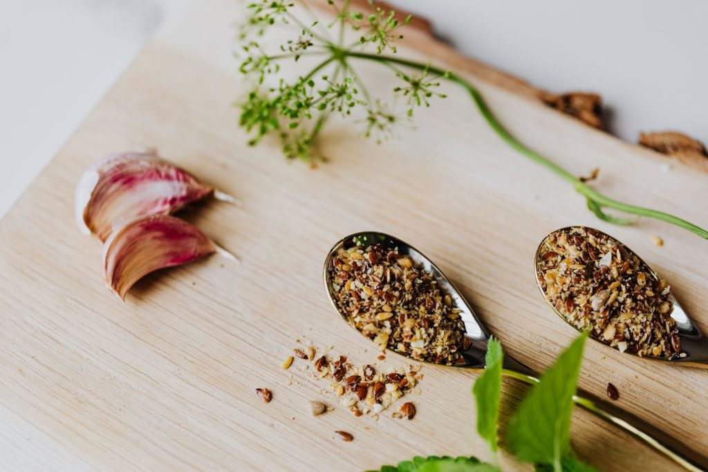A close-up of herbs and spices on a wooden board with garlic and fresh greens.