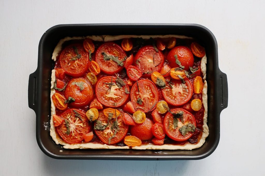 Delicious homemade tomato tart with fresh herbs in a baking pan, perfect for food photography.