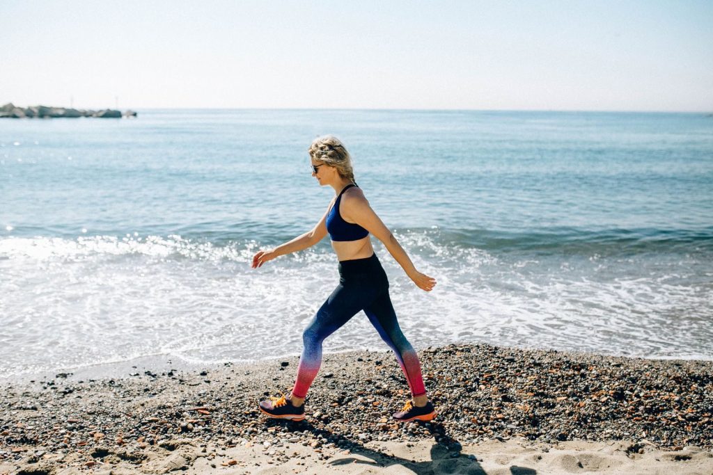 A woman in activewear power walks along a sunny beach shore, enjoying the healthy lifestyle and ocean view.