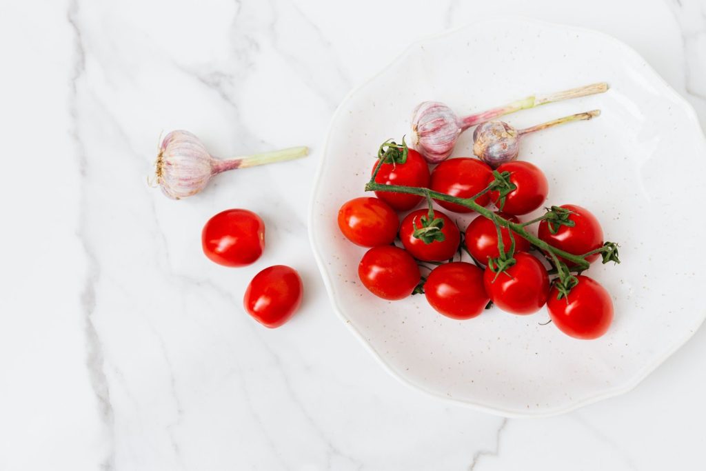 A vivid still life of cherry tomatoes and garlic on a white plate, perfect for culinary themes.