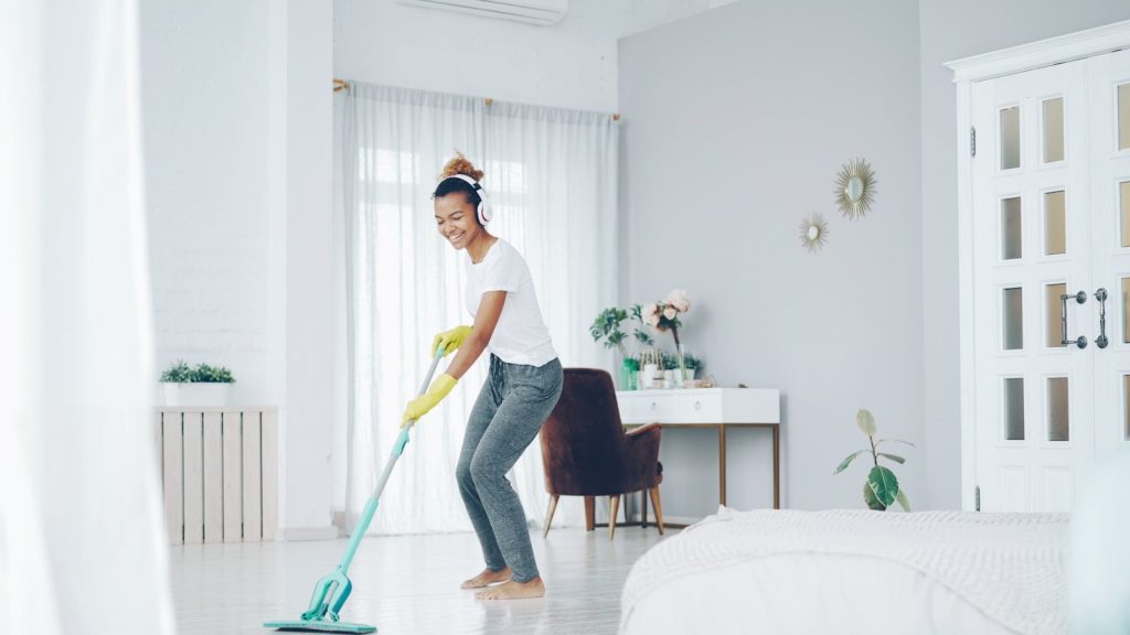 Woman happily mopping the floor in a bright room.