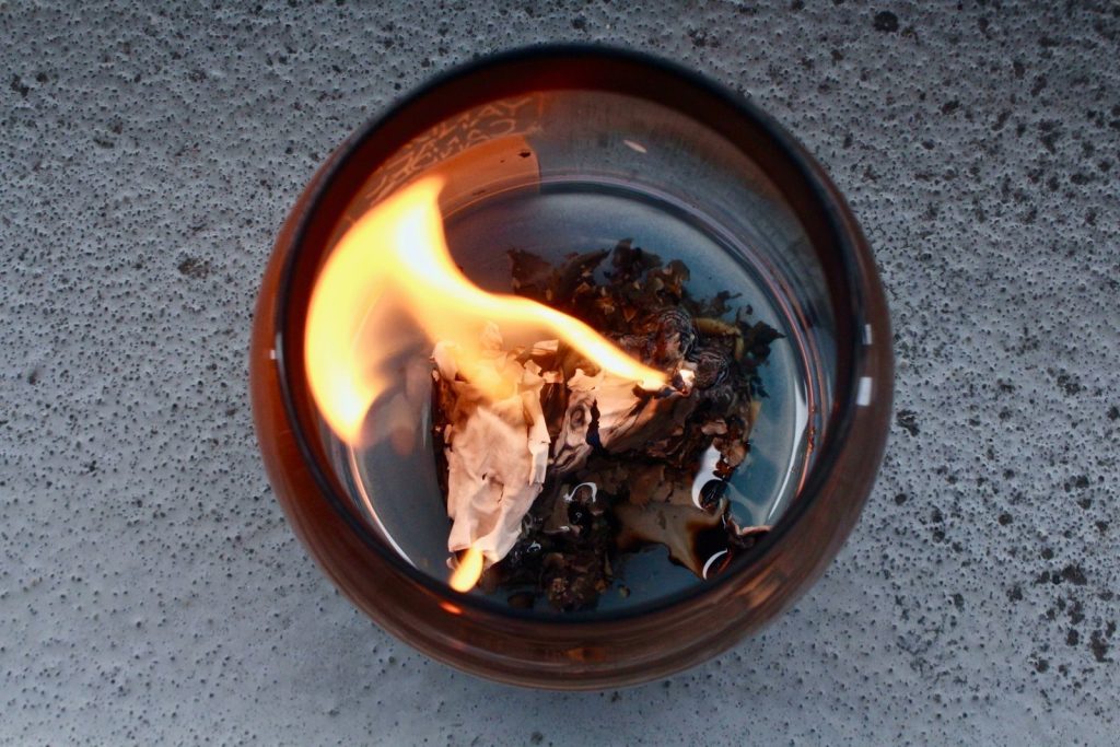 A close-up of paper burning inside a glass container showing a fiery flame.