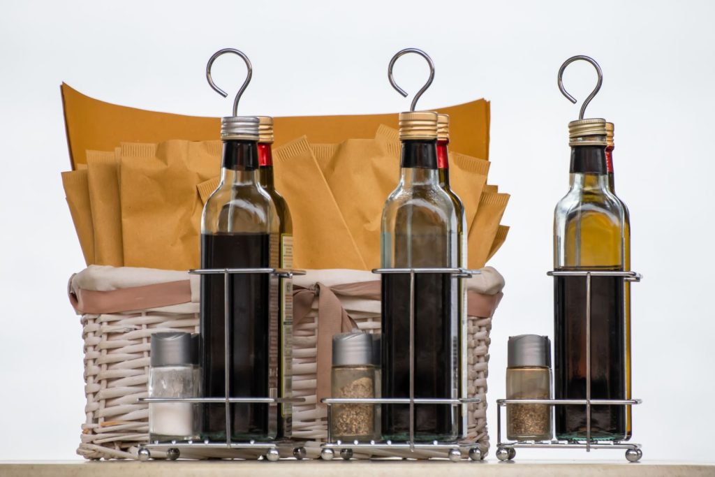 A collection of glass bottles with condiments and spices in a wicker basket.