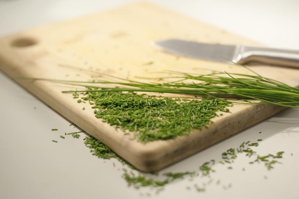 Close-up of fresh chives on a chopping board with a knife, ideal for culinary themes.
