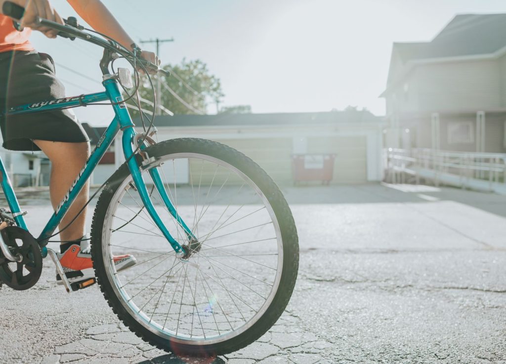 Teen biking along an urban street with sunlight, focusing on teal bicycle and vibrant atmosphere.