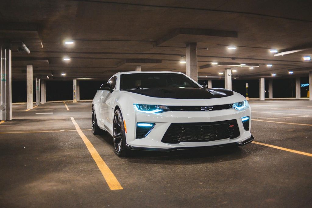 Expensive modern car with glowing headlights on asphalt public parking under roof with luminous lamps at night