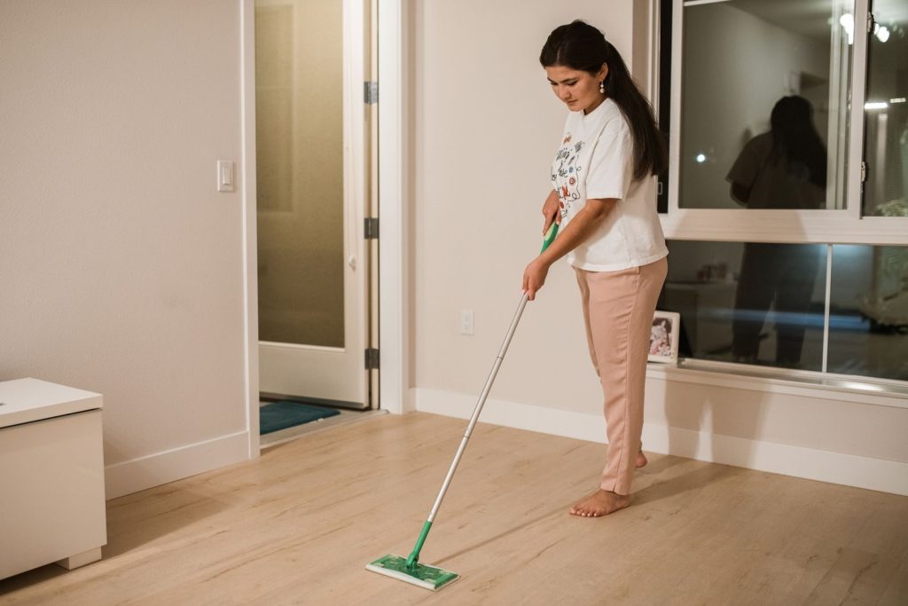 Woman cleaning a room with a mop, demonstrating domestic chores in a minimalist indoor setting.