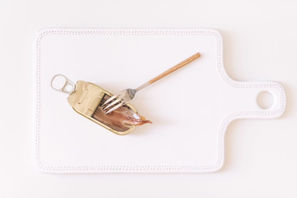 A minimalist top view of canned anchovies on a cutting board with a fork.