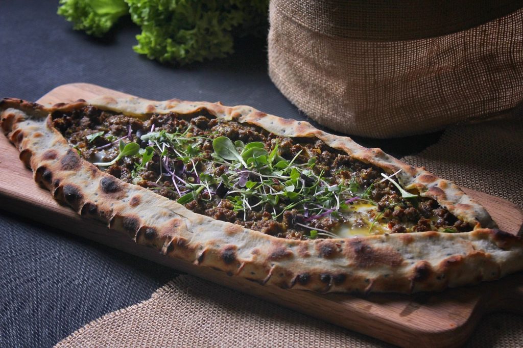 A freshly baked Turkish pide topped with ground meat and fresh greens, presented on a wooden board.