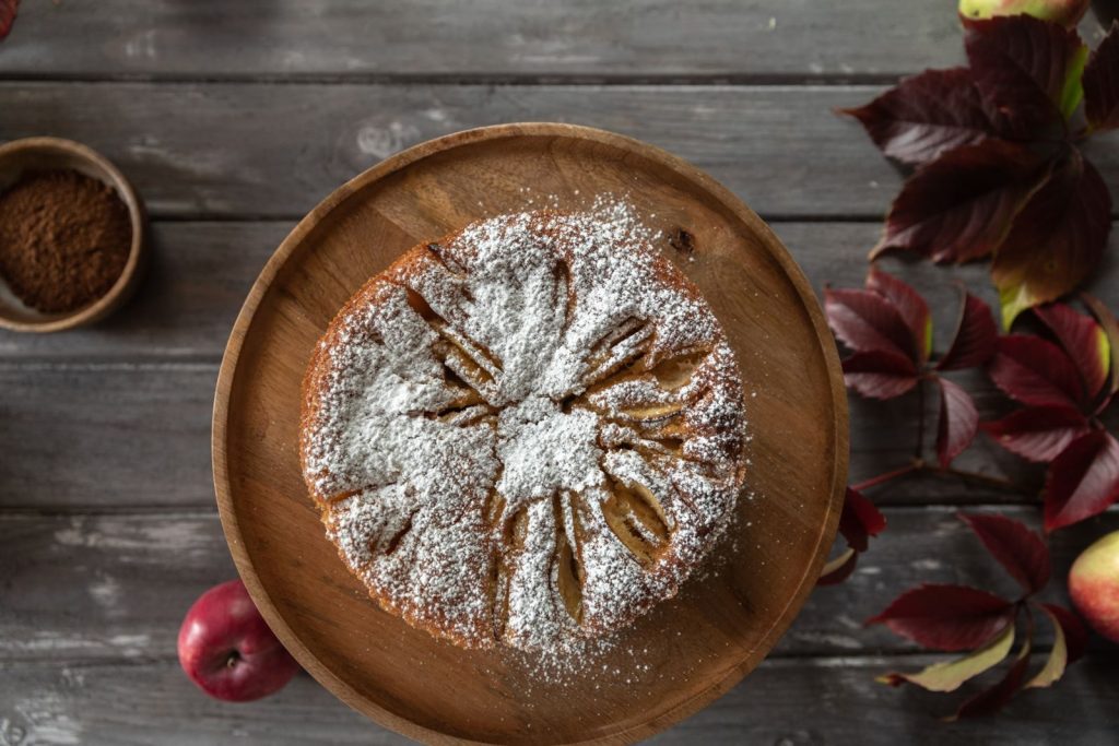 Delicious homemade apple cake topped with powdered sugar on a wooden plate.