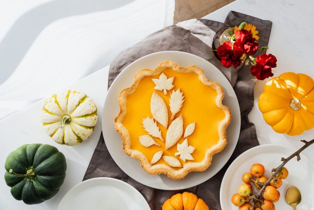 A beautifully styled pumpkin pie surrounded by autumn-themed decorations and mini pumpkins.