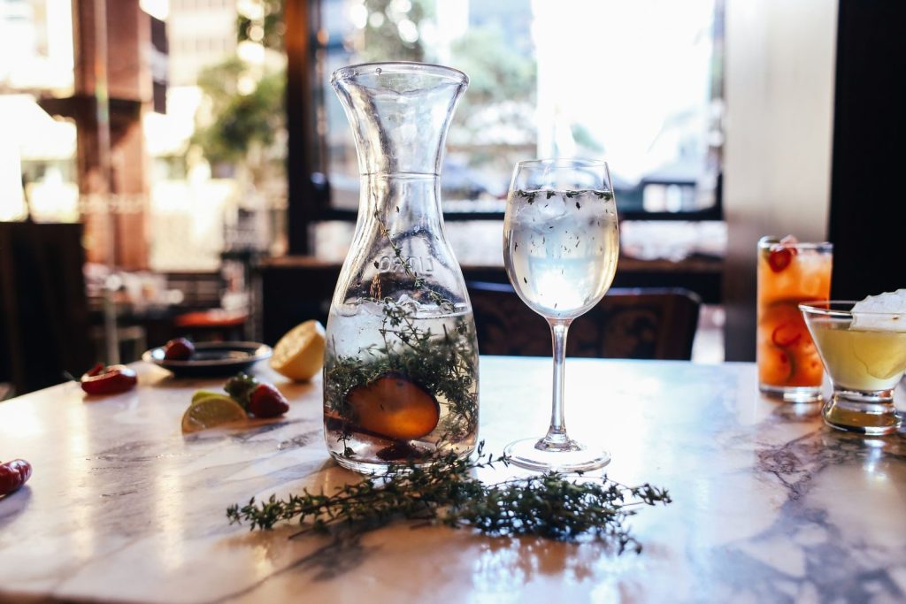 Elegant carafe and cocktail on a marble table with fresh fruits in a modern restaurant setting.