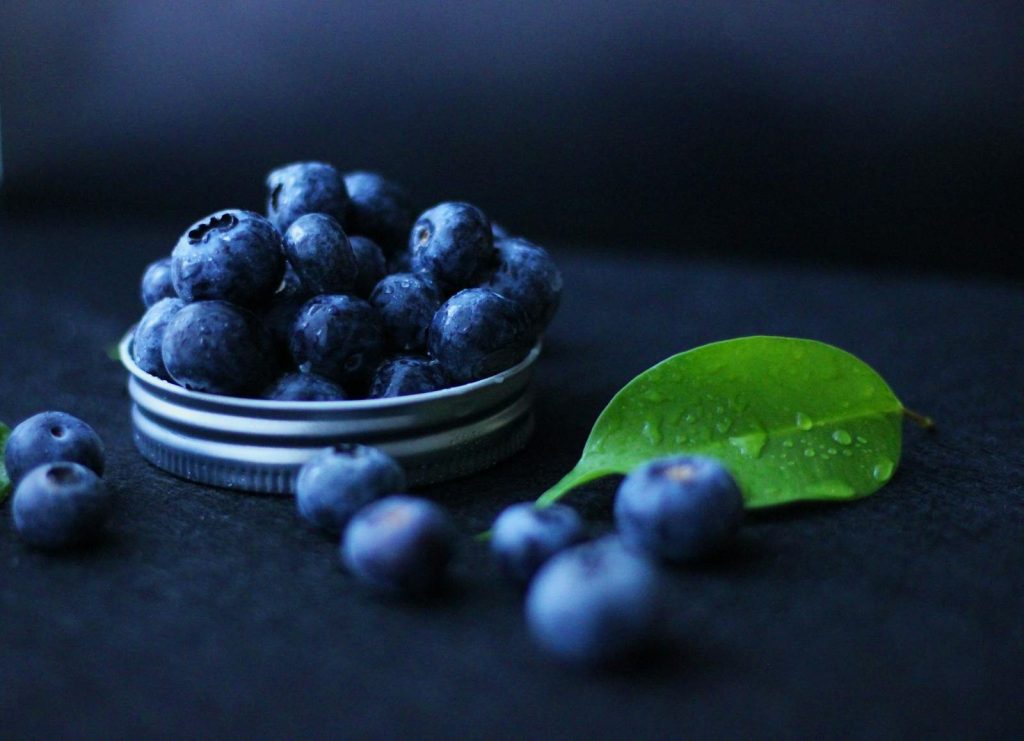 A close-up view of fresh blueberries with a green leaf on a dark background.
