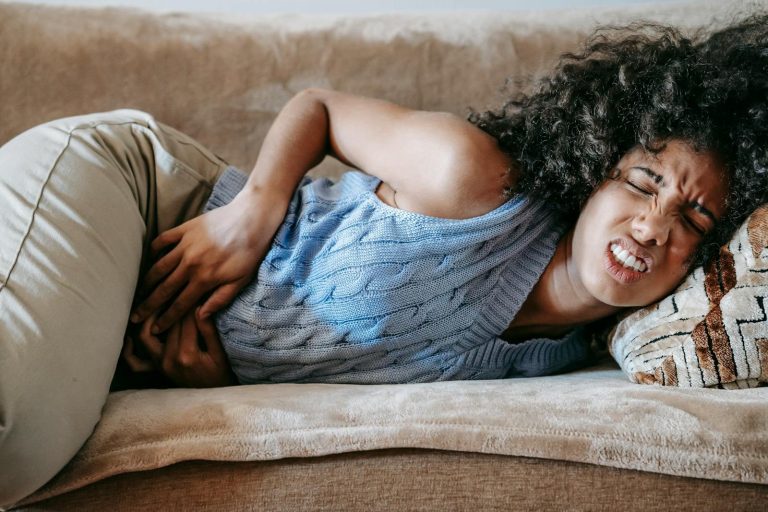 Young African American female lying on sofa in agony while having acute stomach ache