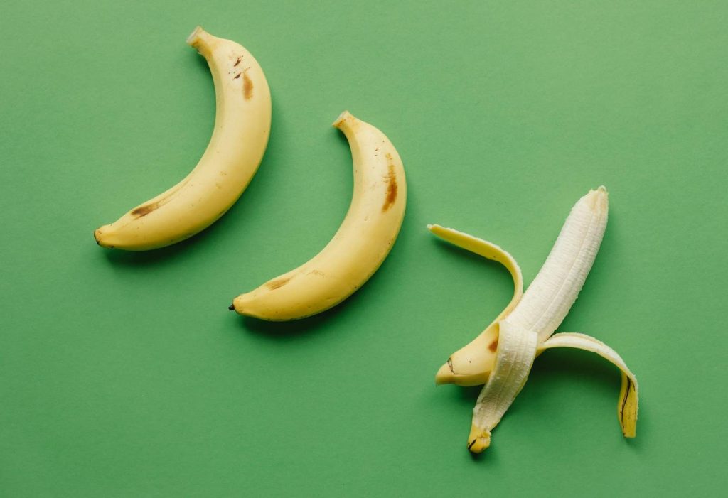 High angle of fresh ripe sweet peeled banana on green background with unpeeled bananas