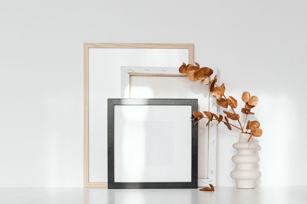 Elegant minimalist composition of picture frames and a white ceramic vase with dried eucalyptus.