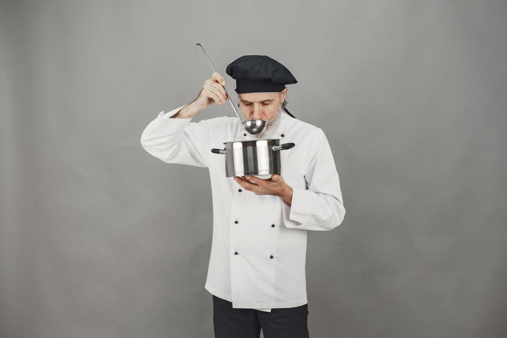 A professional chef tastes food from a pot, showcasing culinary expertise in a modern kitchen setting.