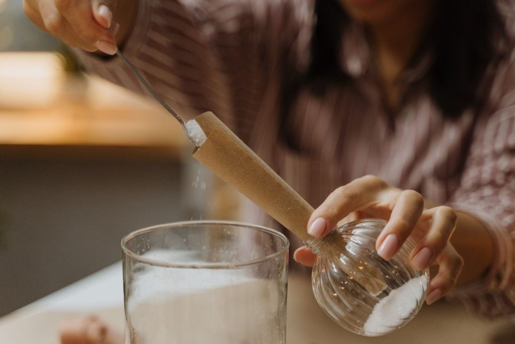 Close-up of a woman using a funnel to pour sugar into a glass. DIY process captured indoors.