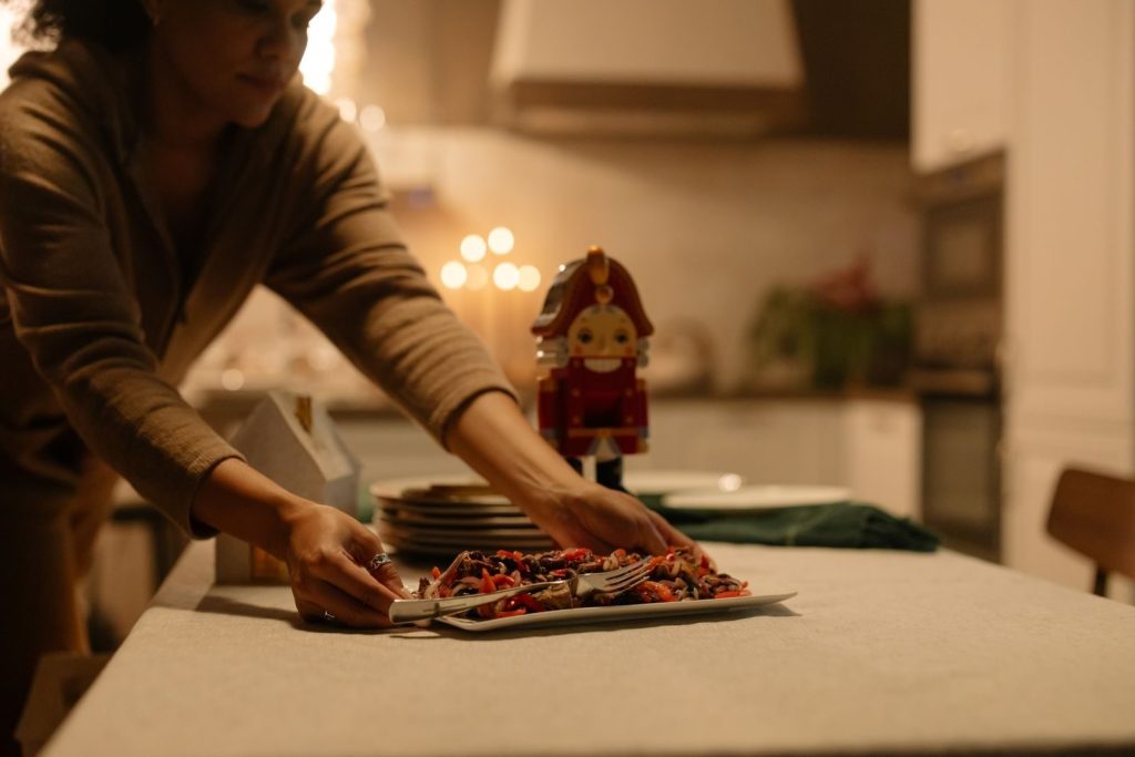 A woman sets a festive dining table with a nutcracker centerpiece during a cozy holiday evening.