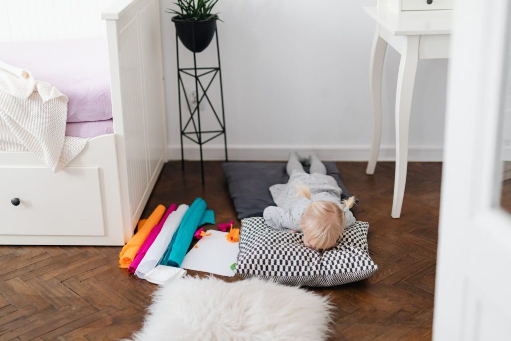 Young child lying on pillow indoors, surrounded by colorful crafts, creating a cozy atmosphere.