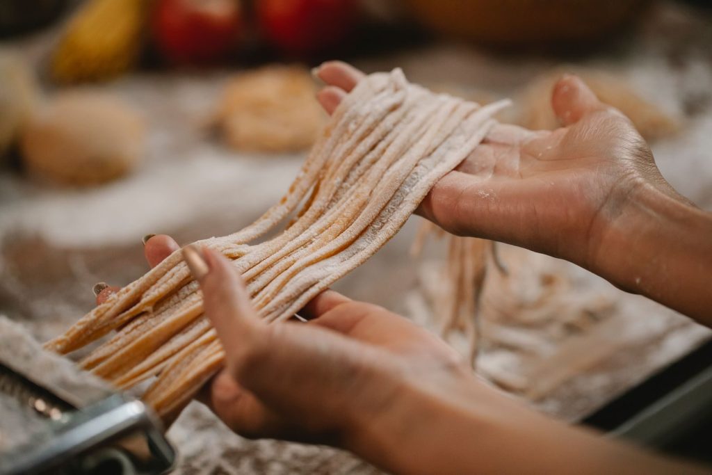 Crop anonymous female producing spaghetti with pasta cutter on blurred background of table