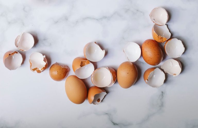 Top view of pile of brown shells and whole eggs scattered on marble table in kitchen on sunny day