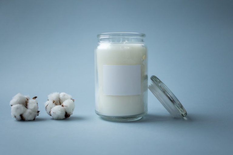 A minimalist shot of a glass jar candle beside cotton balls on a soft blue backdrop.