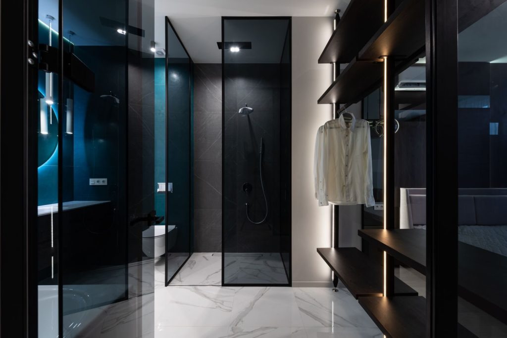Modern wardrobe with wooden shelves in bedroom near bathroom with glass walls in trendy minimalist apartment