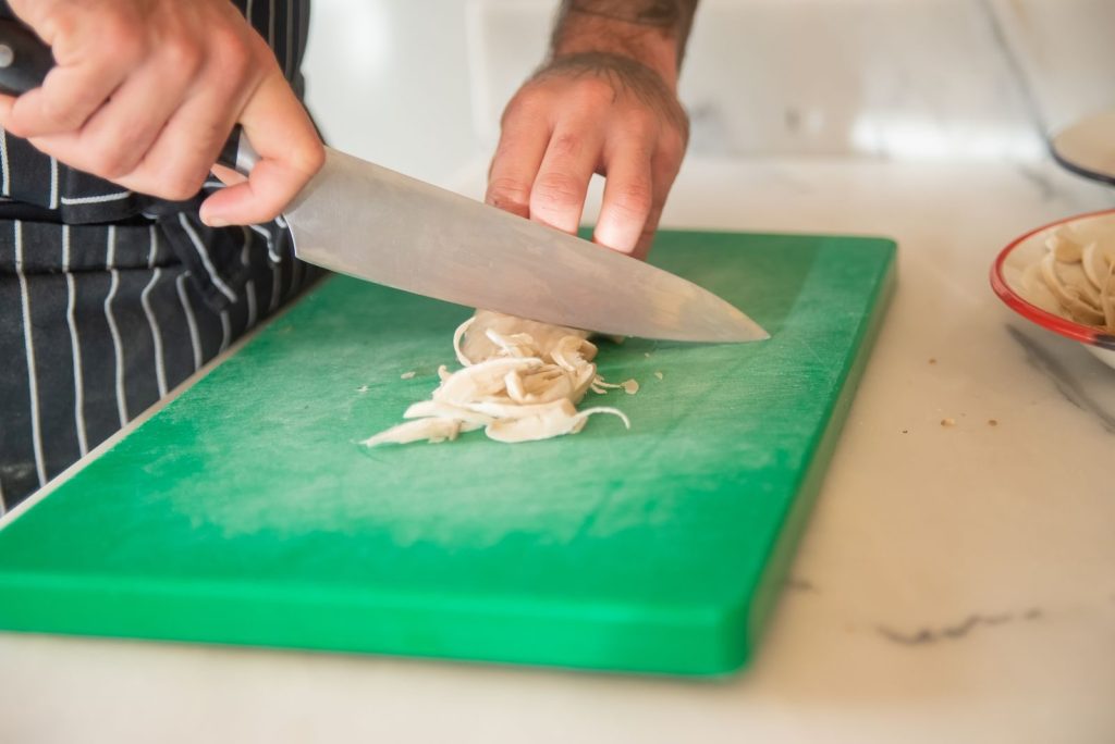 Close-up of a chef slicing mushrooms on a green cutting board, focusing on hands and knife.