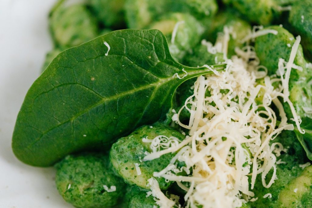 Close-up of spinach gnocchi topped with fresh spinach leaf and grated parmesan cheese.