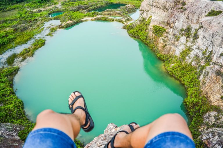 A daring perspective of legs dangling over a cliff with a lake below, perfect for adventure themes.